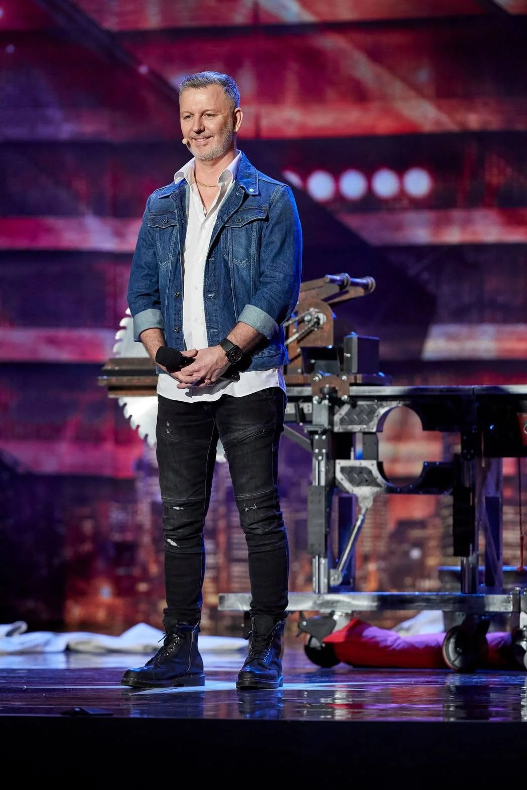 John Taylor standing on a colourful stage holding a microphone