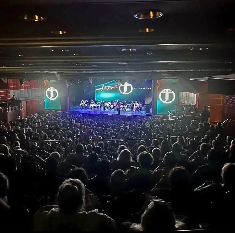 John Taylor on stage before a full audience during a comedy hypnosis show