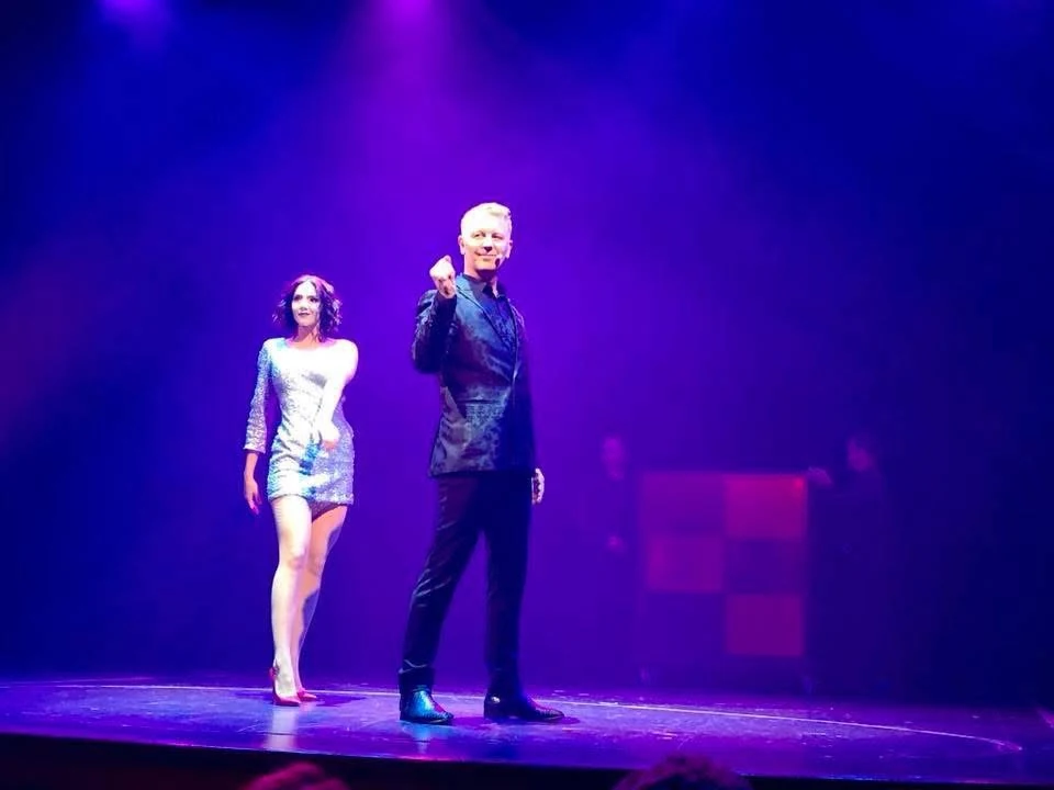 John Taylor and a fellow performer taking a bow under purple theatre lighting